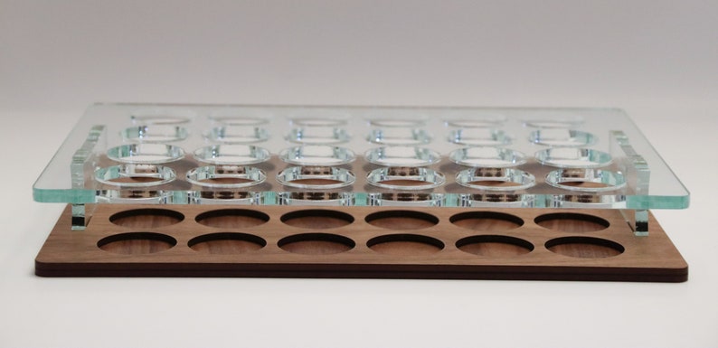 May include: A wooden tray with a clear glass top. The tray has 24 circular cutouts for holding small items. The tray is made of walnut wood and has a natural finish.