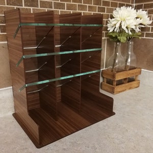 Puede incluir: Un organizador de madera marr&oacute;n con estantes de vidrio y m&uacute;ltiples compartimentos. El organizador est&aacute; sobre una encimera de color gris claro.