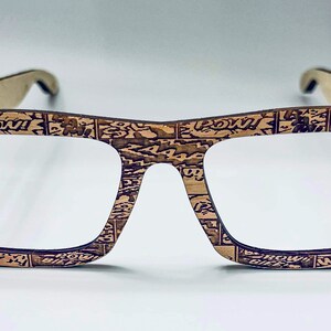 Puede incluir: Un par de gafas con montura de madera marr&oacute;n con un dise&ntilde;o de impresi&oacute;n de c&oacute;mic. Las lentes son transparentes y las monturas tienen una forma cuadrada.