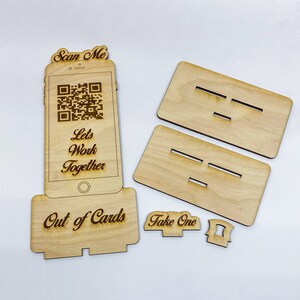 Op de afbeelding: Houten bord met een QR-code, de tekst "Scan Me", "Let's Work Together" en "Out of Cards". Er zijn ook twee houten borden met de tekst "Take One" en een klein houten stuk met een gleuf.