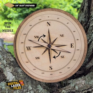 May include: A wooden compass with a brown background and black markings. The compass face reads "Spin the Needle" and has the cardinal directions N, S, E, W, NE, NW, SE, and SW. The compass is made of 1/8 inch plywood.