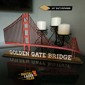 Puede incluir: Un modelo de madera del Golden Gate Bridge, con un puente rojo y soportes negros. El puente está sobre una base de madera con las palabras "Golden Gate Bridge" en letras blancas. El modelo está hecho de madera contrachapada de 1/4 de pulgada de grosor.