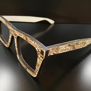 Puede incluir: Un par de gafas de madera marr&oacute;n con un patr&oacute;n de c&oacute;mic. Las gafas tienen un puente nasal de pl&aacute;stico blanco.