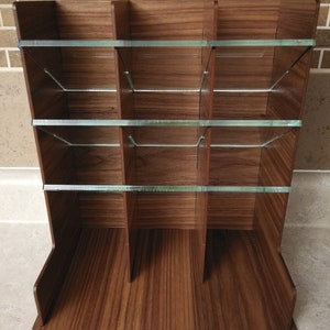 Puede incluir: Un organizador de madera con m&uacute;ltiples compartimentos y estantes de vidrio. El organizador est&aacute; hecho de madera oscura con un patr&oacute;n de veta natural.