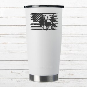 K&ouml;nnte beinhalten: Ein wei&szlig;er Edelstahlbecher mit einem schwarz-wei&szlig;en Design eines Hirsches, der vor einer abgenutzten amerikanischen Flagge mit B&auml;umen und einem Vollmond steht.