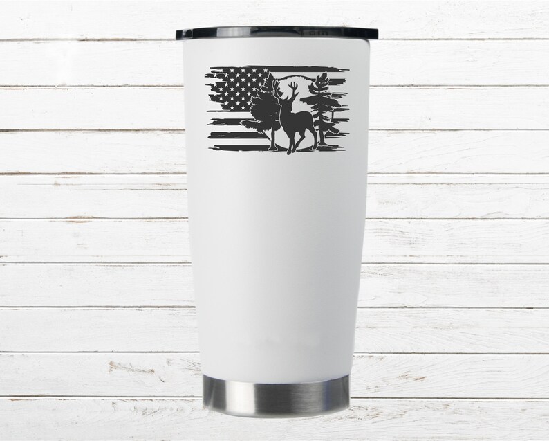 K&ouml;nnte beinhalten: Ein wei&szlig;er Edelstahlbecher mit einem schwarz-wei&szlig;en Design eines Hirsches, der vor einer abgenutzten amerikanischen Flagge mit B&auml;umen und einem Vollmond steht.