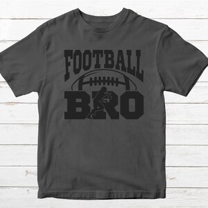May include: A dark gray t-shirt with the text "FOOTBALL BRO" in black lettering. A football and a football player are depicted in the design.