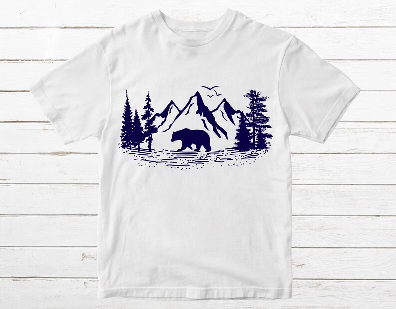 May include: White t-shirt with a navy blue silhouette of a bear walking in front of mountains and trees.