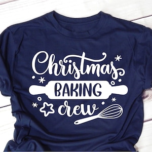 Może przedstawiać: Koszulka w kolorze granatowym z białym napisem "Christmas Baking Crew". Tekst jest otoczony śnieżynkami i zawiera wałek do ciasta i trzepaczkę.
