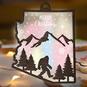 May include: Wooden Christmas decoration in the shape of Arizona, with a mountain range, fir trees, a Bigfoot silhouette, and the words "Merry Christmas." The background has a pastel colour scheme with stars and a snowflake.