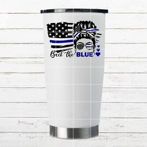 Puede incluir: Un vaso blanco con un dise&ntilde;o de bandera estadounidense azul y blanca, una cara de mujer con un mo&ntilde;o y gafas de sol, y el texto "Back the BLUE" con corazones.