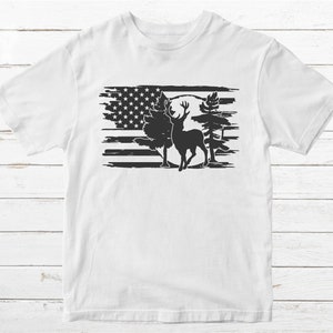 K&ouml;nnte beinhalten: Wei&szlig;es T-Shirt mit einer schwarz-wei&szlig;en Grafik eines Hirsches, der vor einer stilisierten amerikanischen Flagge steht.