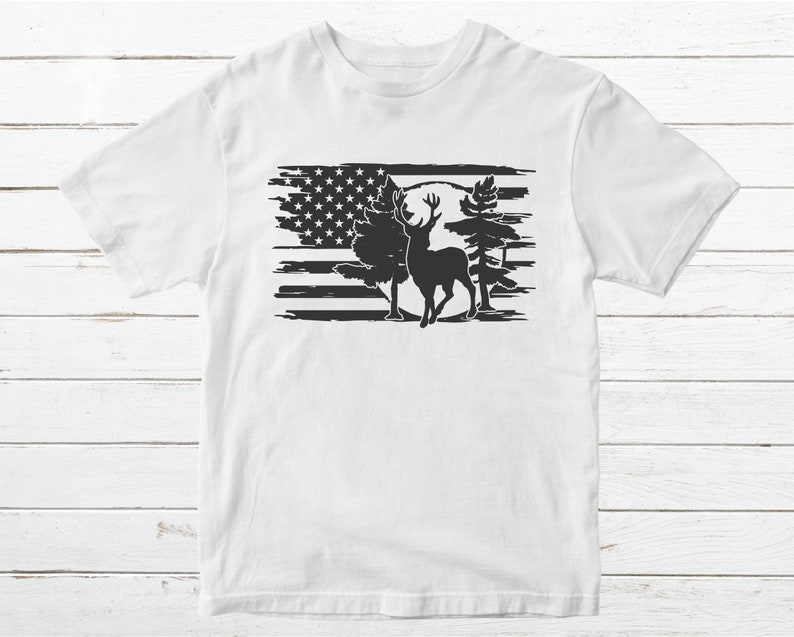 K&ouml;nnte beinhalten: Wei&szlig;es T-Shirt mit einer schwarz-wei&szlig;en Grafik eines Hirsches, der vor einer stilisierten amerikanischen Flagge steht.