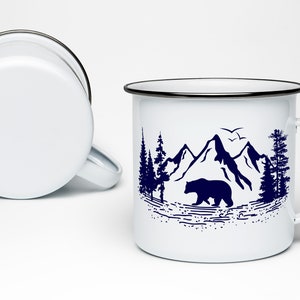 May include: White enamel mug with a black rim and handle. The mug features a blue silhouette design of a bear walking through a mountain landscape with trees.