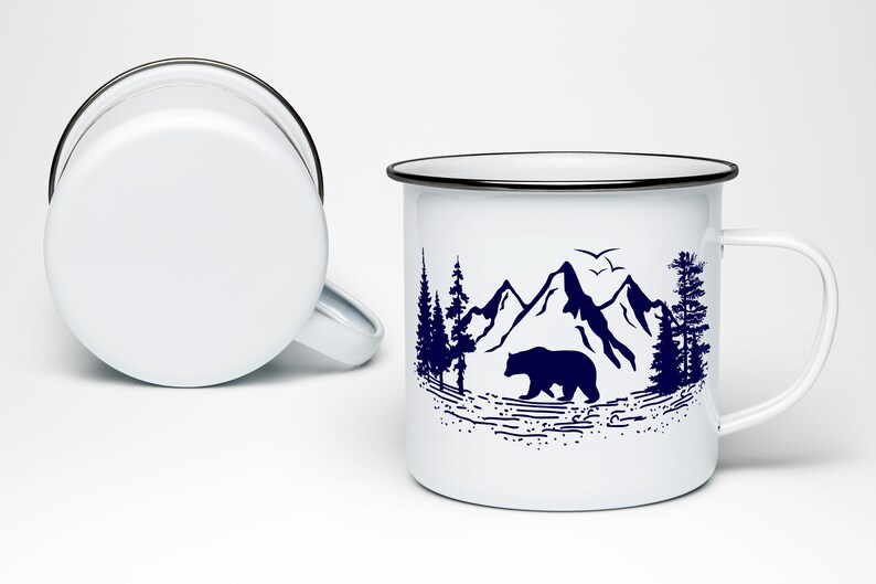 May include: White enamel mug with a black rim and handle. The mug features a blue silhouette design of a bear walking through a mountain landscape with trees.