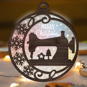 May include: A wooden Christmas ornament shaped like a sewing machine with a white "Merry Christmas" inscription. The ornament has a gradient background with snowflakes and stars.
