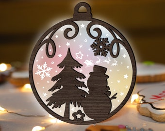 May include: A wooden Christmas ornament shaped like a ball with a brown woodgrain finish. The ornament features a white silhouette of a Christmas tree, a snowman, and snowflakes. The ornament has a white background with a pink and blue ombre effect.