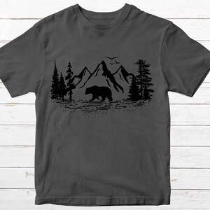May include: A dark gray t-shirt with a black silhouette of a bear walking through a mountain range with trees on either side.
