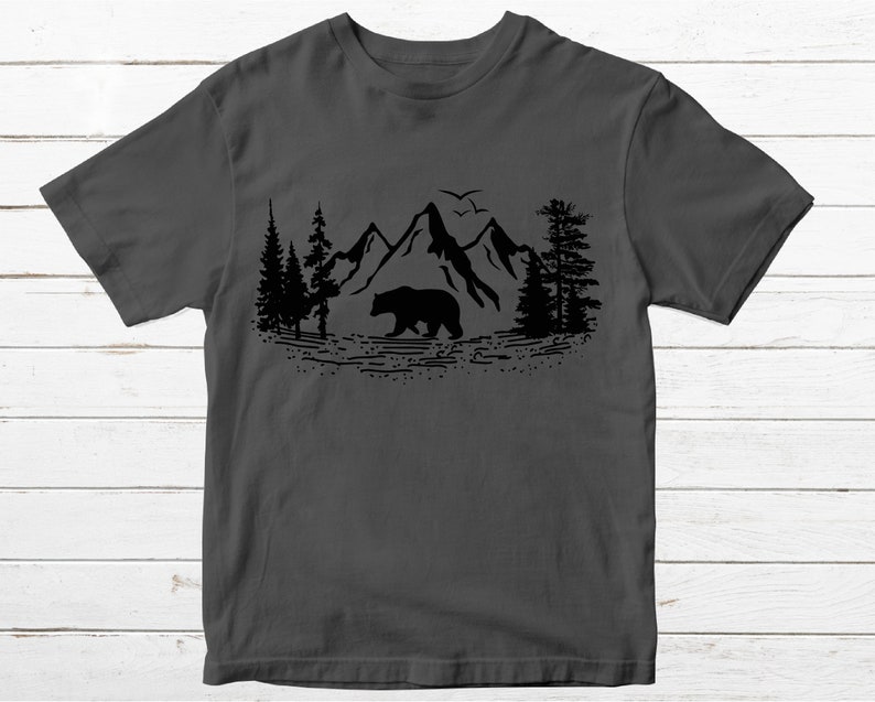 May include: A dark gray t-shirt with a black silhouette of a bear walking through a mountain range with trees on either side.