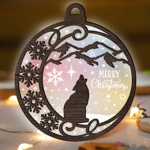 May include: A wooden Christmas ornament shaped like a circle with a wolf silhouette inside. The ornament has a snowy mountain scene with a star and snowflakes. The text "Merry Christmas" is written on the ornament.