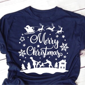 May include: A navy blue t-shirt with a white design featuring a family with a dog, a snowman, a house, and reindeer pulling Santa's sleigh. The text "Merry Christmas" is written in a festive font.