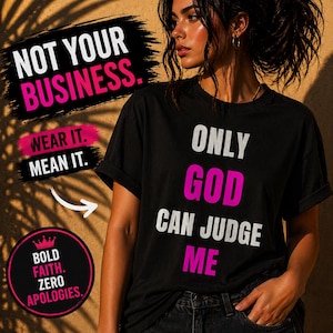 Op de afbeelding: Zwart T-shirt met de tekst "ONLY GOD CAN JUDGE ME" in wit en roze. Het shirt heeft ook de zinnen "NOT YOUR BUSINESS", "WEAR IT. MEAN IT." en "BOLD FAITH. ZERO APOLOGIES." in een grafisch ontwerp.