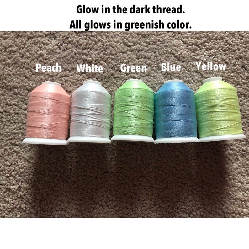 Może przedstawiać: Pięć szpulek nici świecących w ciemności w kolorach brzoskwiniowym, białym, zielonym, niebieskim i ż&oacute;łtym. Tekst "Glow in the dark thread. All glows in greenish color." znajduje się nad szpulkami.