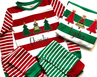 May include: Red and green striped pajamas with a Christmas tree design and the name "Charlie" embroidered on the top. The pajamas also include a matching top with the name "Lydia" embroidered on it.