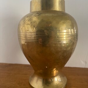 May include: A gold brass vase with a round body and a flared base. The vase has a smooth, polished finish and a subtle, textured pattern.