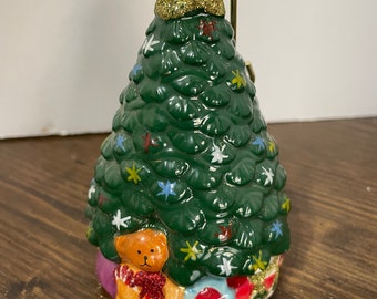 May include: A ceramic Christmas tree ornament with a green tree, gold glitter, and a teddy bear with presents at the base.