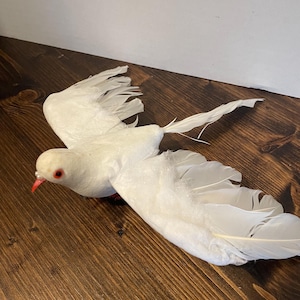 May include: A white dove figurine with red eyes, in flight with its wings spread wide. The dove is made of soft, fluffy material and has realistic feathers.