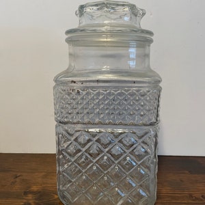 Op de afbeelding: Een glazen pot met een diamantpatroon en een deksel. De pot is leeg.