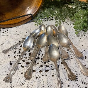 May include: A collection of silver spoons with ornate handles, arranged on a white crocheted doily.