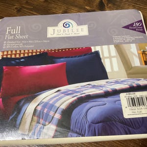 May include: Full size flat sheet in a cream and blue plaid pattern. The sheet is made of 50% cotton and 50% polyester and has an 180 thread count. The sheet is shown on a bed with a blue comforter and red and blue pillows.