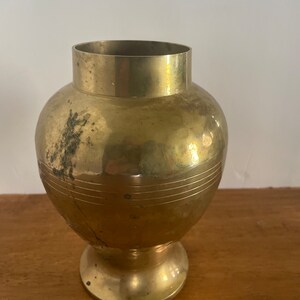 May include: A gold brass vase with a round body and a flared base. The vase has a smooth, polished finish and a subtle, textured pattern.