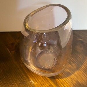 May include: A clear glass vase with a unique, organic shape. The vase has a wide opening and a rounded bottom.