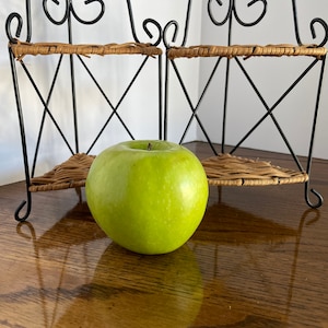 May include: Two black metal shelves with woven wicker tops, a green apple sits on the table in front of the shelves.