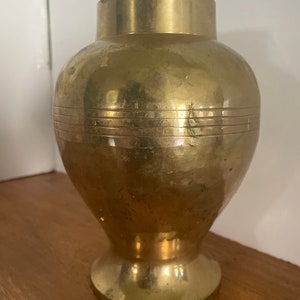 May include: A gold metal vase with a round body and a flared base. The vase has a smooth, polished finish and a subtle sheen.