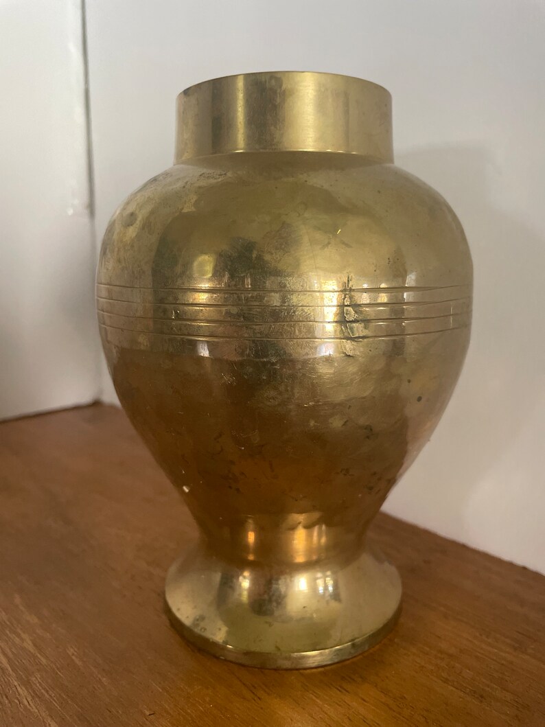 May include: A gold metal vase with a round body and a flared base. The vase has a smooth, polished finish and a subtle sheen.