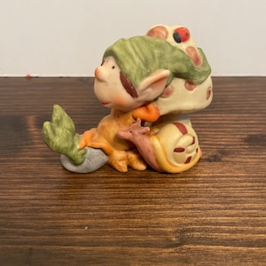 Könnte beinhalten: Eine Keramikfigur eines grünen Kobolds, der einen Pilzhut mit einem Marienkäfer auf der Oberseite trägt. Der Kobold sitzt auf einer Schnecke mit einer braunen Schale.