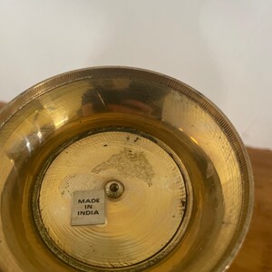 May include: The bottom of a gold metal vase with a sticker that reads "Made in India".