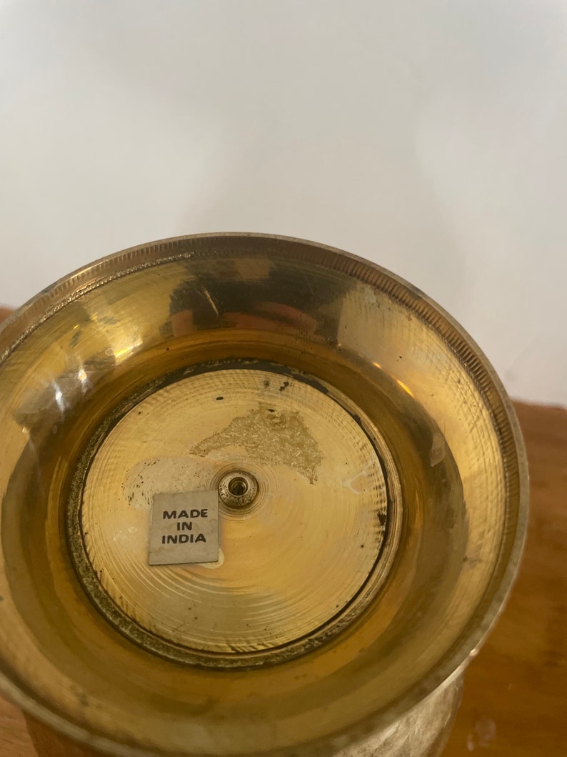 May include: The bottom of a gold metal vase with a sticker that reads "Made in India".