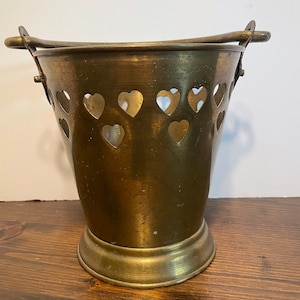 May include: A brass bucket with heart-shaped cutouts and two handles. The bucket has a gold finish and a round base.