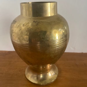 May include: A gold metal vase with a round body and a flared base. The vase has a smooth, polished finish.