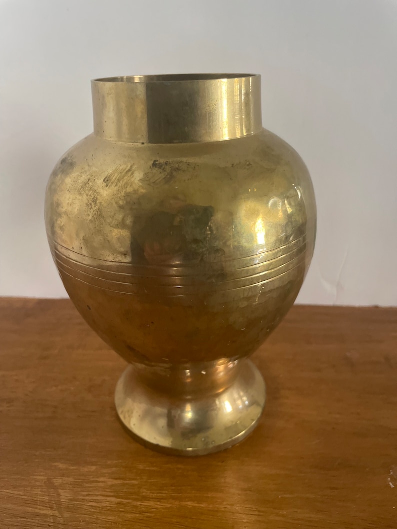 May include: A gold metal vase with a round body and a flared base. The vase has a smooth, polished finish.