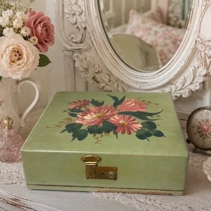 May include: A rectangular sage green wooden box with a hinged lid featuring a hand-painted floral design of pink and red flowers with dark green leaves. The box includes a gold-toned metal latch mechanism on the front center for closure.