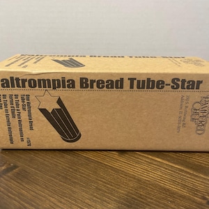 May include: A brown cardboard box with the text "altrompia Bread Tube-Star" printed in black. The box also features a star and tube graphic. The Pampered Chef logo is visible on the right side of the box.