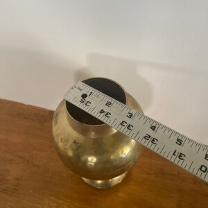May include: A gold metal vase with a round body and a flared base. The vase is approximately 3.5 inches tall.