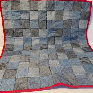 May include: A patchwork quilt made from denim fabric in shades of blue and grey. The quilt is edged with a red border.