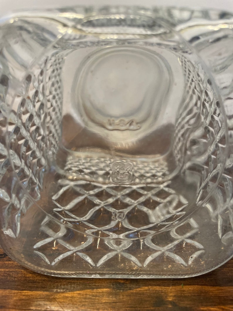 Op de afbeelding: Een heldere glazen fles met een diamantpatroon op de bodem. De fles heeft een vierkante vorm en een brede opening.